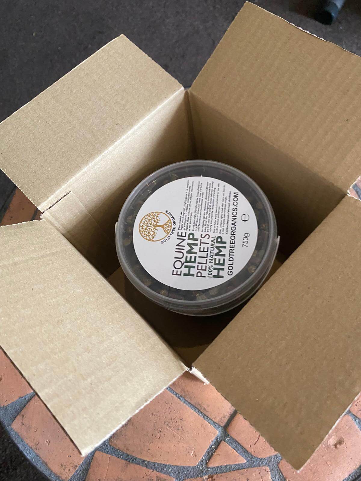 Open cardboard box containing Gold Tree Organics equine hemp pellets in a sealed container
