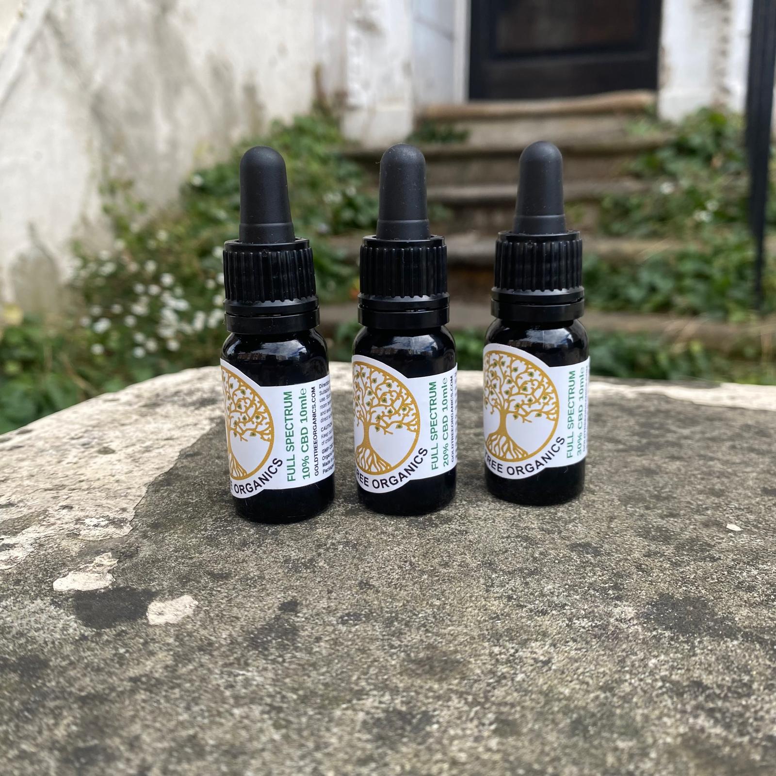 Three bottles of Gold Tree Organics full spectrum CBD oil on a stone surface outdoors