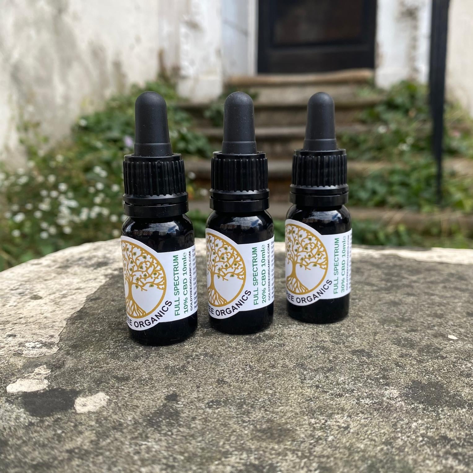 Three bottles of Gold Tree Organics full spectrum CBD oil placed on a stone surface outdoors